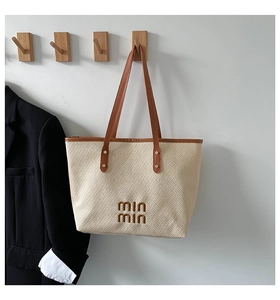 Detail of cream woven tote bag with brown leather handles and embroidered logo