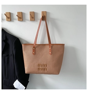 Detail shot of woven tote bag texture with brown leather straps and metal logo