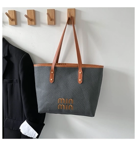 Detail view of woven grey tote bag with brown leather handles and golden rivets