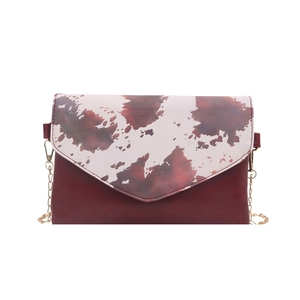 Red brown envelope bag with cow print flap and gold chain strap on white background