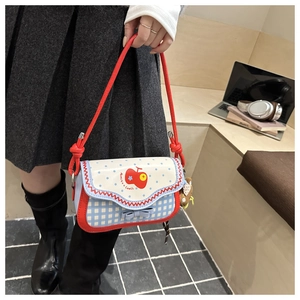 Close-up of pink apple handbag with red bow, plush bear charm, and polka dot flap detail