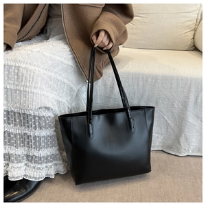 Chic black leather tote bag shown with a brown coat and white skirt in a cozy setting