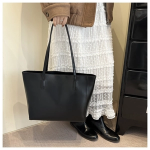 Detailed view of minimalist black leather tote bag worn with a brown stylish coat