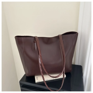 Detail view of a large dark brown tote bag displayed on a sleek black glossy pedestal