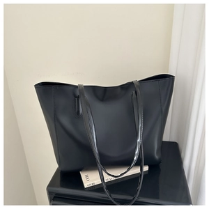 Detail of minimalist large black tote bag in PU leather on a polished black surface
