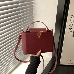 Burgundy faux leather bucket bag with gold V-shaped buckle and top handle shown on model