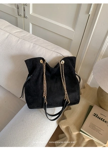 Detail of black suede bucket bag with gold chain strap and drawstring closure