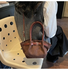 Brown suede handbag shown in a lifestyle setting with crossbody strap and leather handle