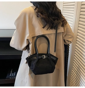 Detail of black suede crossbody bag with metal buckle worn with a beige trench coat