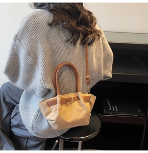 Detail view of beige suede handbag with brown leather handles and decorative buckle