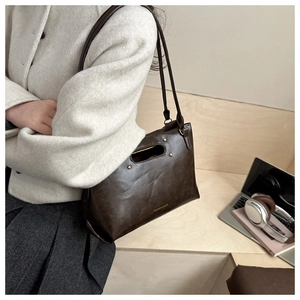 Detail of dark brown leather tote featuring unique hollow handle and metal rivet accents