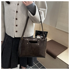 Close-up of a dark brown faux leather handbag featuring gold studs and hollow handle