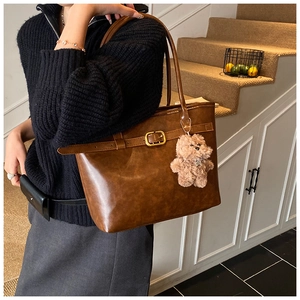 Brown vintage leather tote bag with buckle detail and plush bear charm shown on shoulder