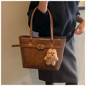 Detail of dark brown leather tote bag with a gold buckle and cute plush bear charm