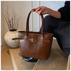 Macro detail of a vintage brown leather tote bag with decorative metal buckle straps
