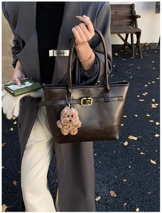 Detail of dark brown tote bag with matte leather texture and cute teddy bear charm