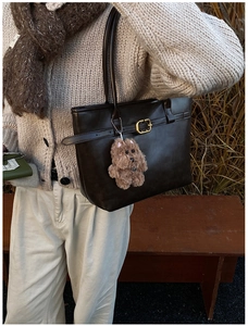 Detail of dark brown leather tote bag with metal buckle and plush puppy charm accessory