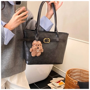 Detail of black matte tote bag with golden buckle and brown plush puppy charm