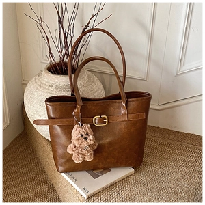 Detail of brown faux leather tote bag with gold buckle and cute plush dog charm