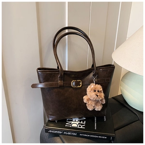 Detail of dark brown leather tote bag with gold buckle and cute plush bear charm