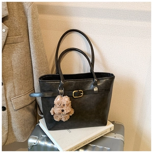 Detail of vintage black tote bag with decorative metal buckle and plush dog charm