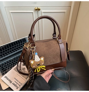 Detail of dark brown boston bag featuring suede texture and a cute plush bear charm