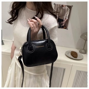 Detail of a black leather pillow bag with gold hardware held by a model in a minimalist room