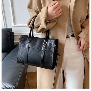 Detail of black crocodile embossed tote bag featuring leather texture and dual handle straps