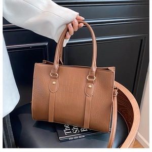 Detail of brown crocodile embossed tote bag with metal rivets and shoulder strap