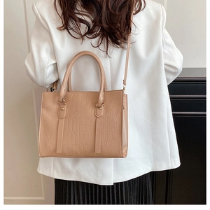 Detailed view of beige crocodile pattern tote bag with gold hardware worn by model