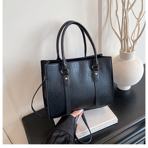 Detail of black crocodile embossed tote bag with metal hardware on a minimalist background