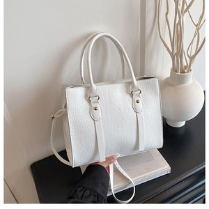 Detail view of white crocodile pattern tote bag with gold studs on a minimalist black surface