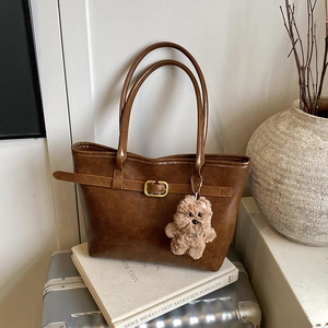 Large brown leather tote bag with gold buckle and puppy charm on vintage suitcase