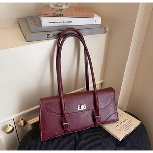 Détail d'un sac sous les bras bordeaux avec fermoir argenté sur des livres anciens
