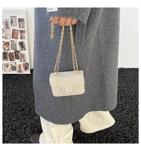 Detail of a mini beige chain bag showing white contrast stitching and gold metal strap