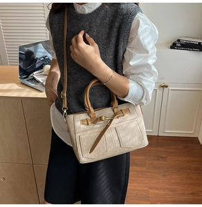 Detail of cream croc-textured tote bag with brown leather trim and metal buckles