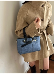 Detail of blue denim shoulder bag with double pockets and premium gold hardware accents