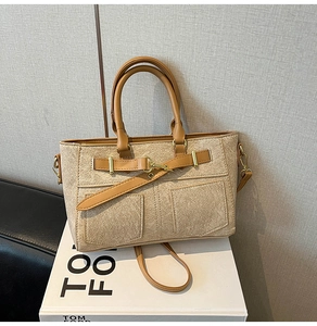 Detail of beige canvas tote with brown leather trim and metal buckle on display