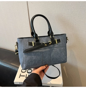 Detail of grey-blue denim handbag featuring black leather straps and gold metal hardware
