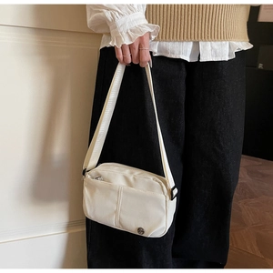 Detail of white nylon crossbody bag featuring a hidden zipper pocket and metal logo