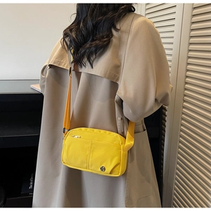 Detail of a yellow nylon crossbody bag featuring multiple zipper pockets and adjustable strap