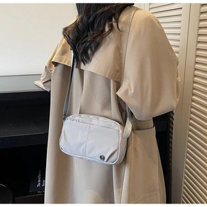Detail of light gray nylon crossbody bag with zipper pocket and metal logo detail