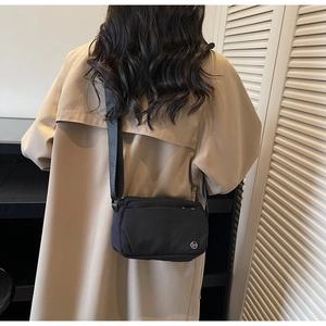 Detail shot of a black nylon crossbody bag worn over a beige coat with wide strap