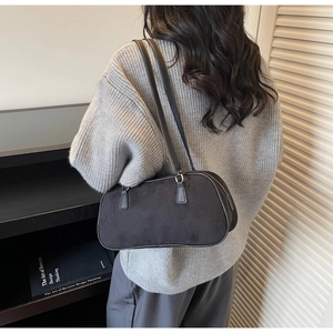 Detailed side view of a black faux suede baguette shoulder bag worn by a model