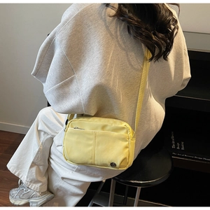 Model wearing a yellow nylon crossbody bag with zipper pocket and adjustable strap