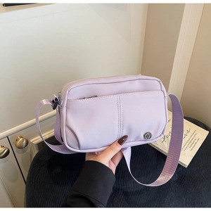 Close-up of light purple crossbody bag with metal logo on dark stool backdrop