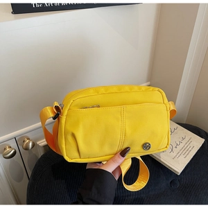 Detail of a bright yellow nylon crossbody bag featuring a metal logo and zip pocket
