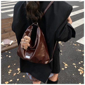 Detail of dark brown glossy backpack with cute plush bear charm on a black blazer