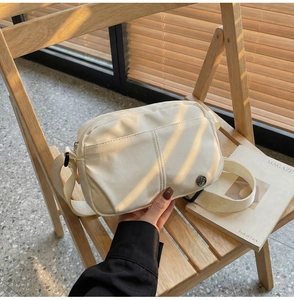 Detail view of a beige nylon crossbody bag on a wooden chair with a wide woven strap