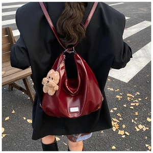Rear view of model wearing burgundy glossy leather backpack with cute bear pendant